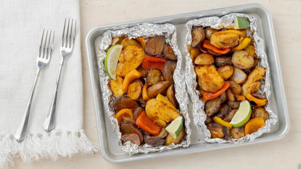 A countertop with a baking sheet on it, and two foil packets full of delicious Little Potatoes and veggies.
