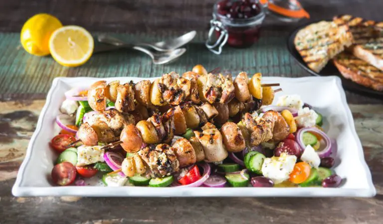 A plate of chicken and veggie kebabs on a bed of Greek salad