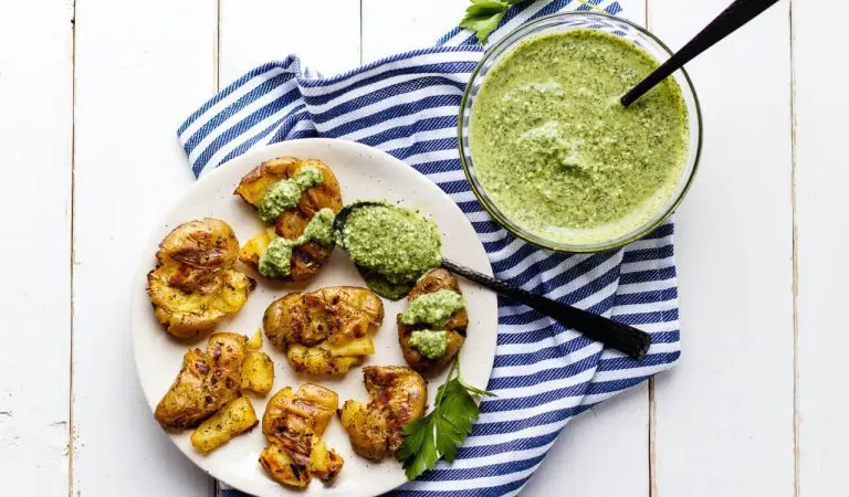 Grilled smashed fingerling potatoes on a plate with some dill dip on the side.