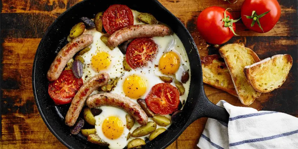 A pan of eggs breakfast sausages and veggies.