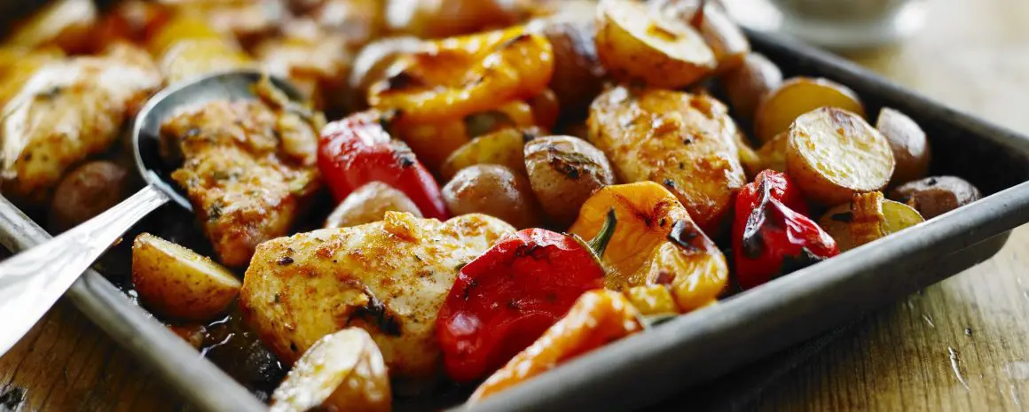 Poulet jerk rôti sur une plaque avec petites pommes de terre et poivrons