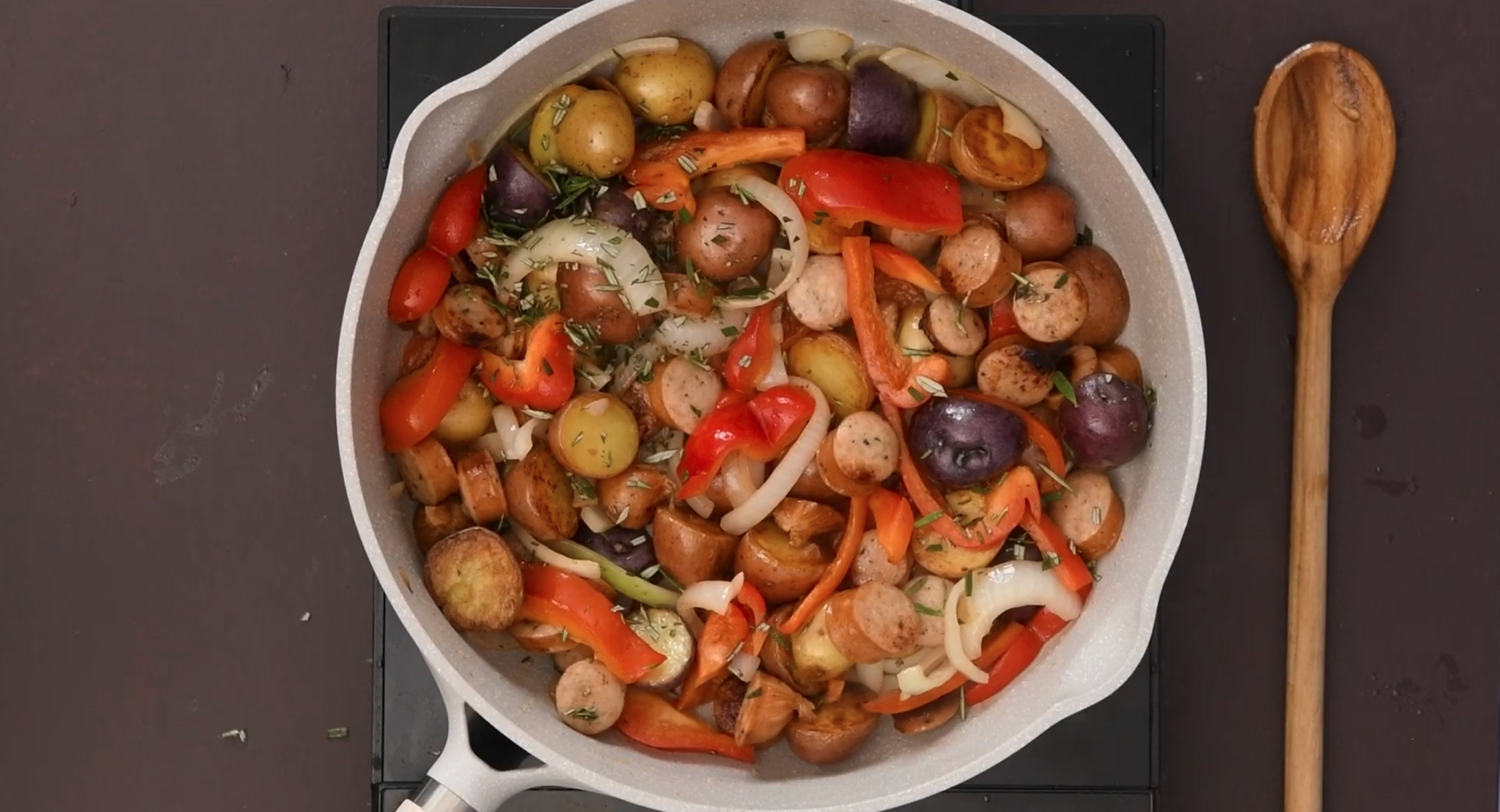 A cast iron skillet full of potatoes, sausages, and peppers.