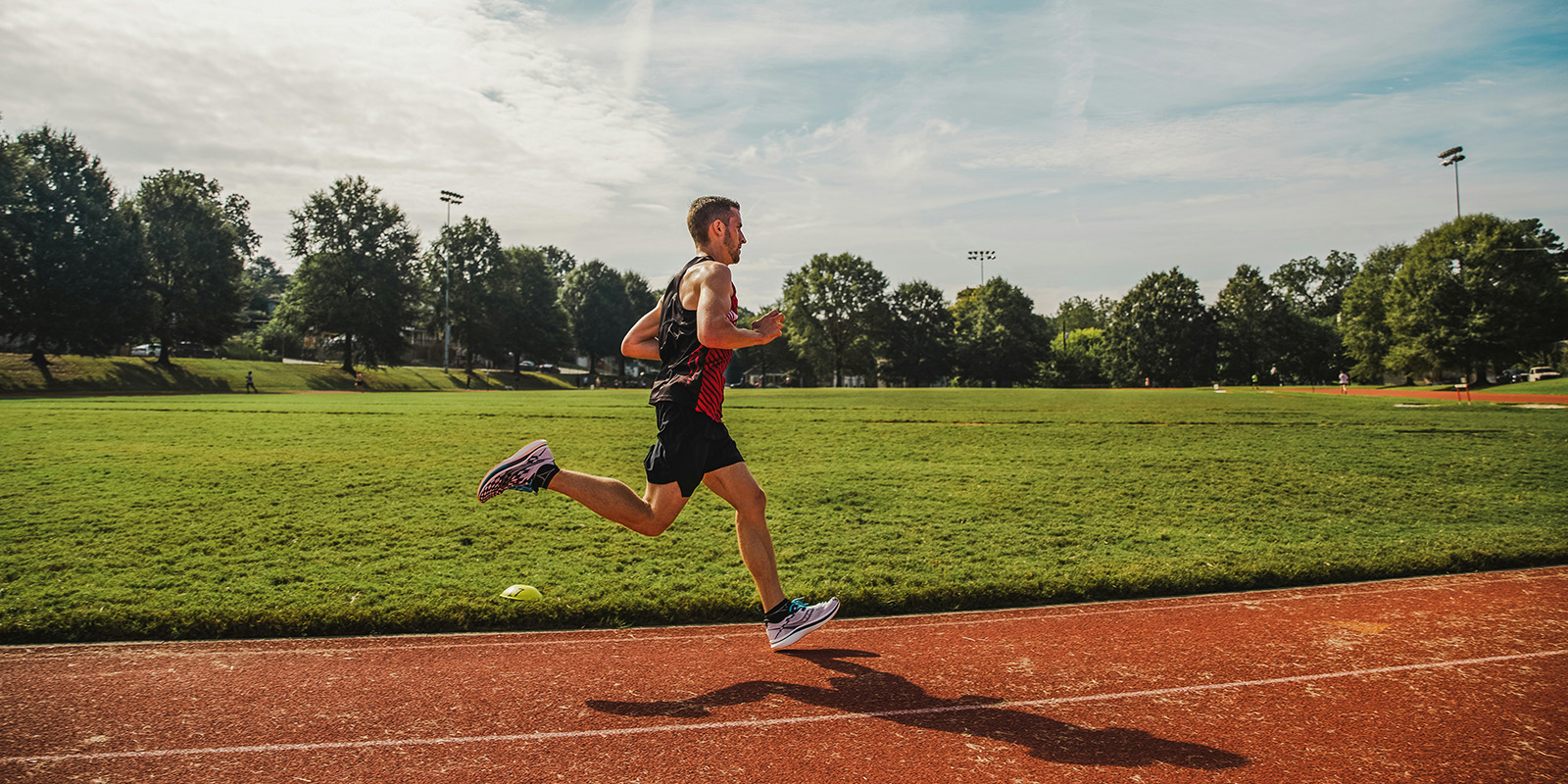 An athlete is running around a track on a sunny day.