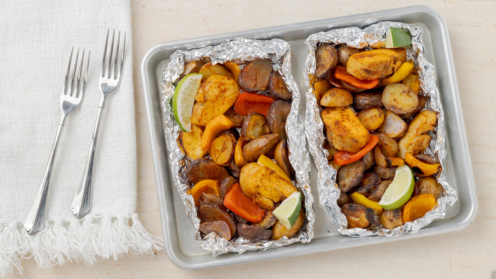 A countertop with a baking sheet on it, and two foil packets full of delicious Little Potatoes and veggies.