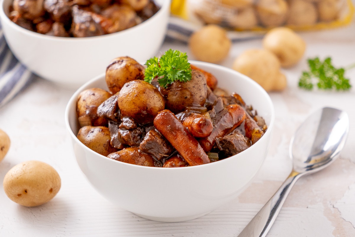 Honey balsamic slow cooker beef stew in a white bowl surrounded by potatoes.