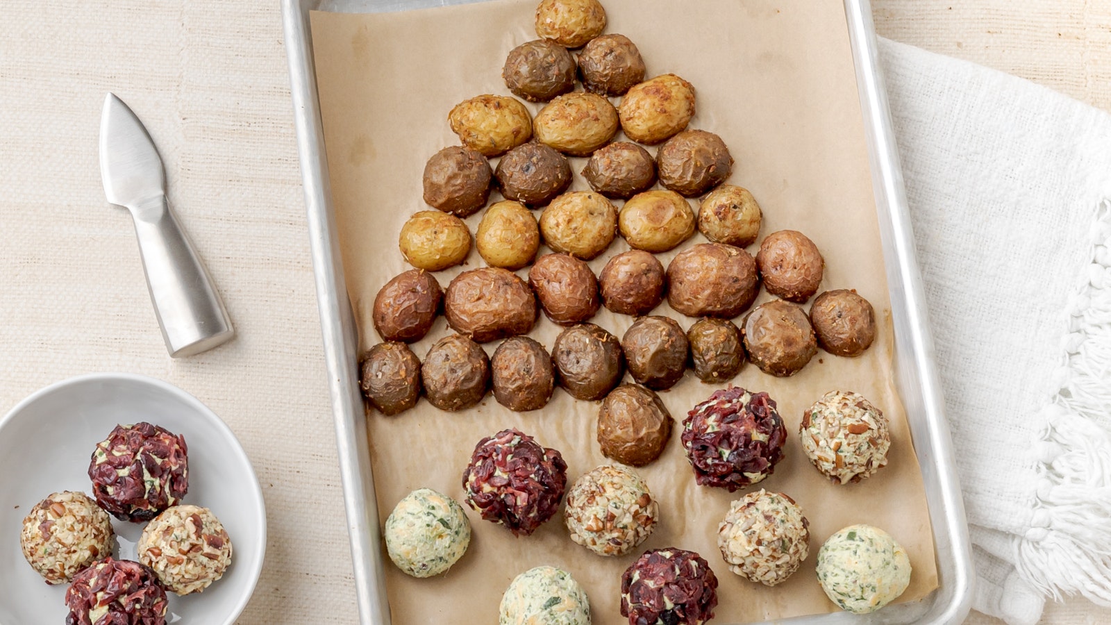 Festive cheese ball coated in herbs and cranberries, served on a holiday platter with roasted Little Potatoes and crackers for dipping.