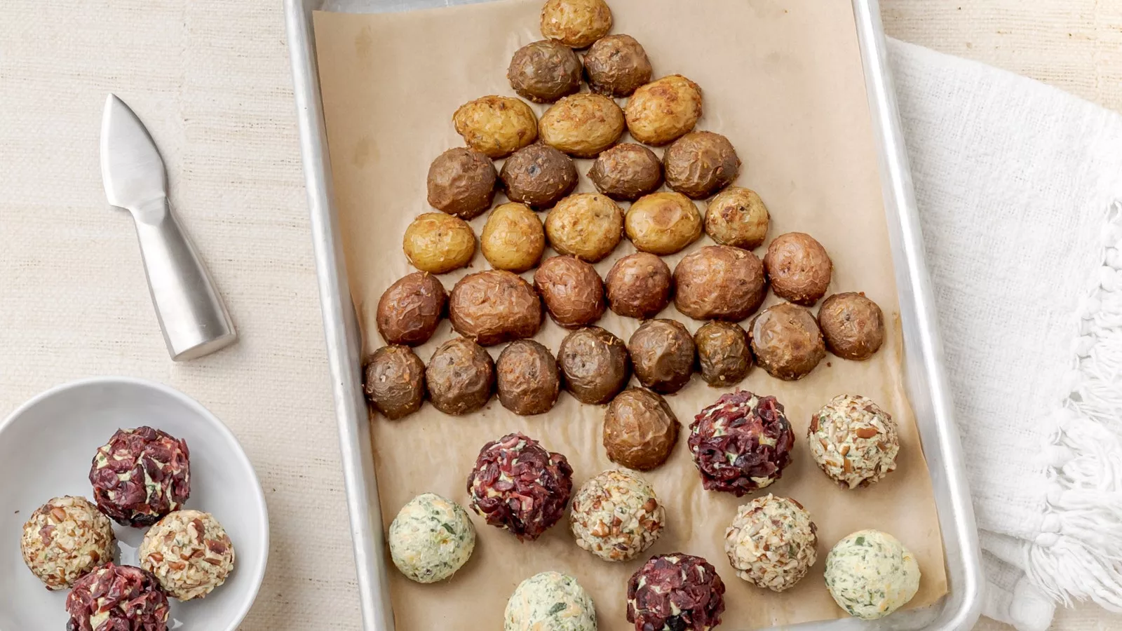 Festive cheese ball coated in herbs and cranberries, served on a holiday platter with roasted Little Potatoes and crackers for dipping.