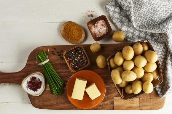Ingredients on a cutting board like Little Potatoes, butter, chives, and pink salt.
