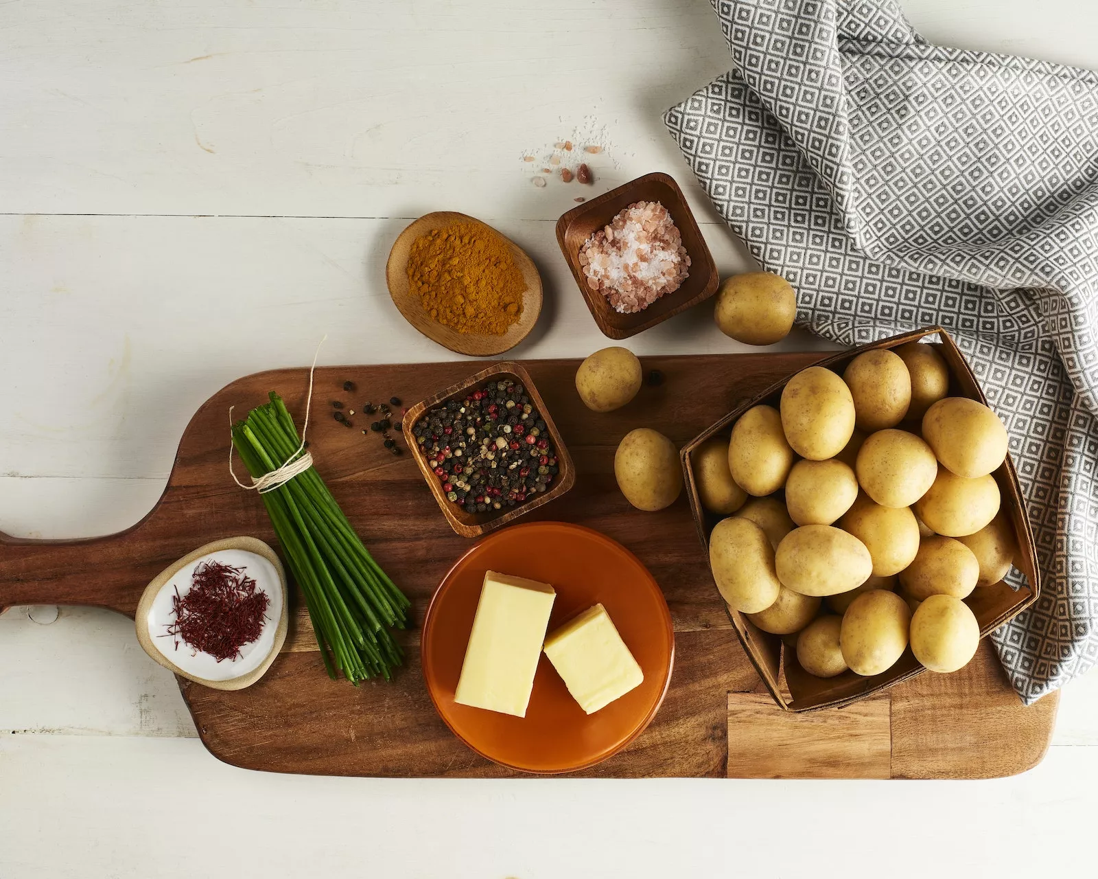 Ingredients on a cutting board like Little Potatoes, butter, chives, and pink salt.