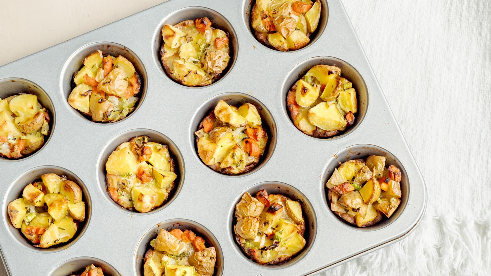 Golden-brown muffin tin potato stuffing cups made with Little Potatoes and herbs, arranged on a white serving platter with fresh thyme and rosemary.