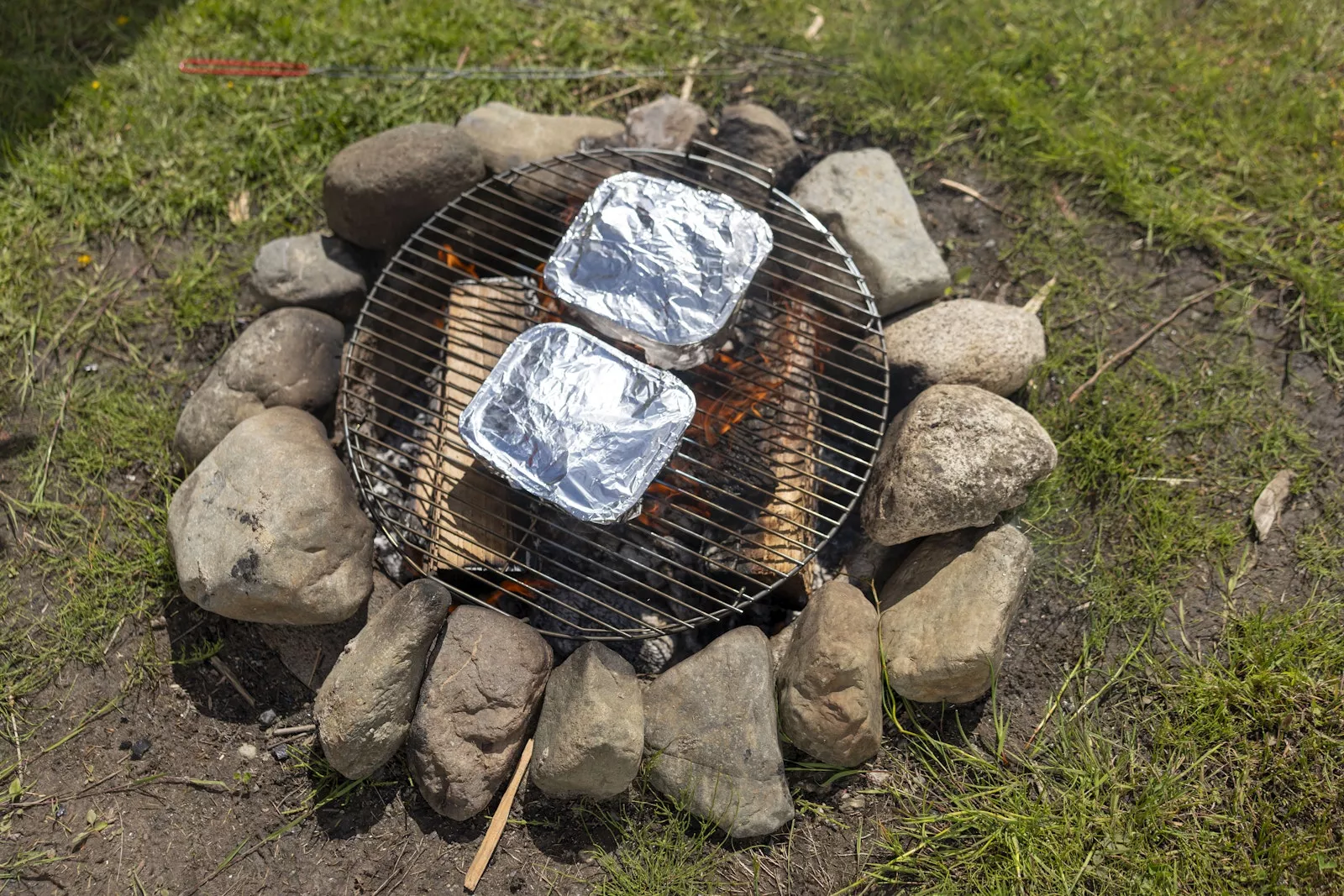 A campfire with a grill over it with foil covered Little Potato trays.