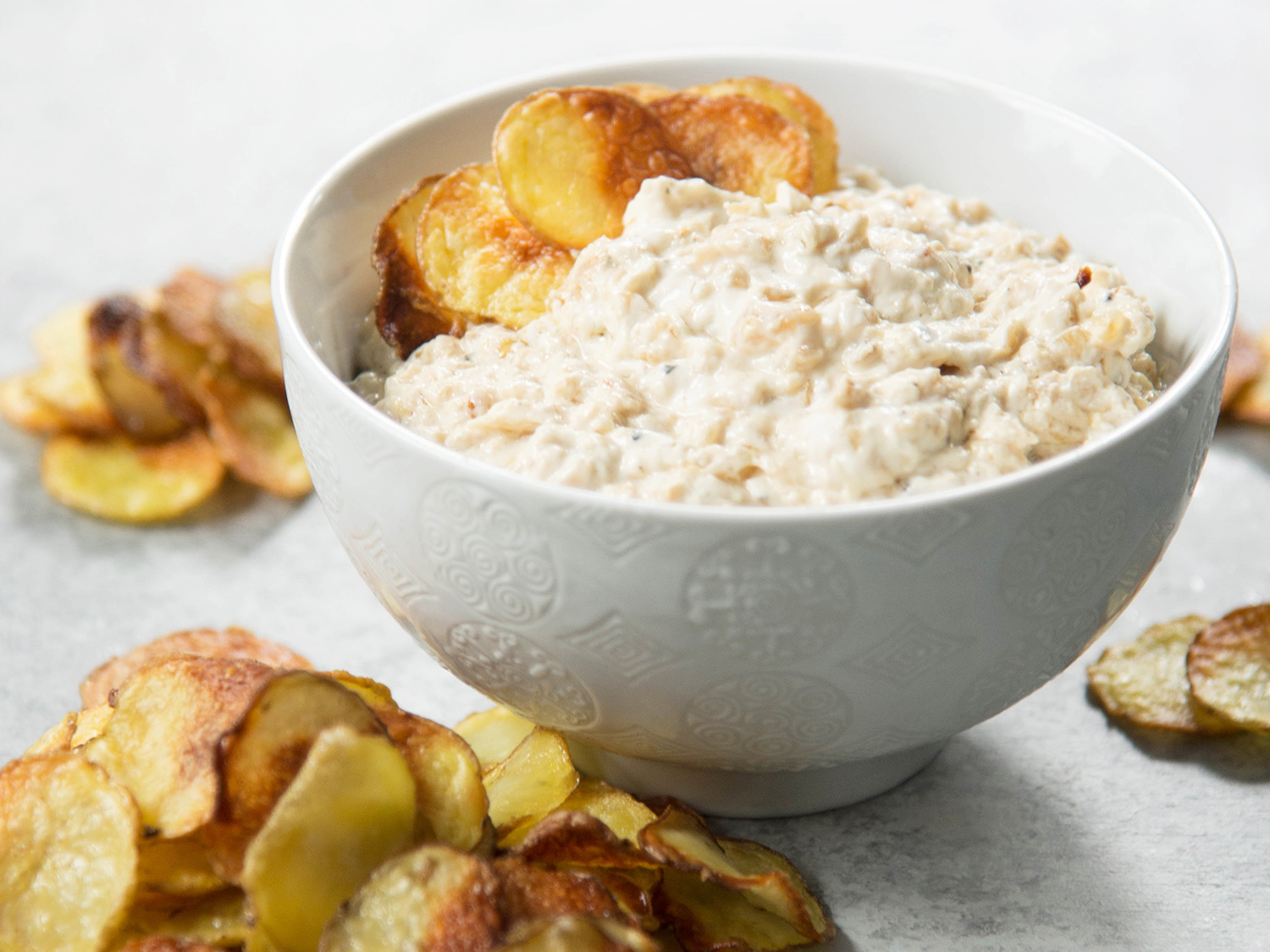 A bowl of onion dip with potato chips.