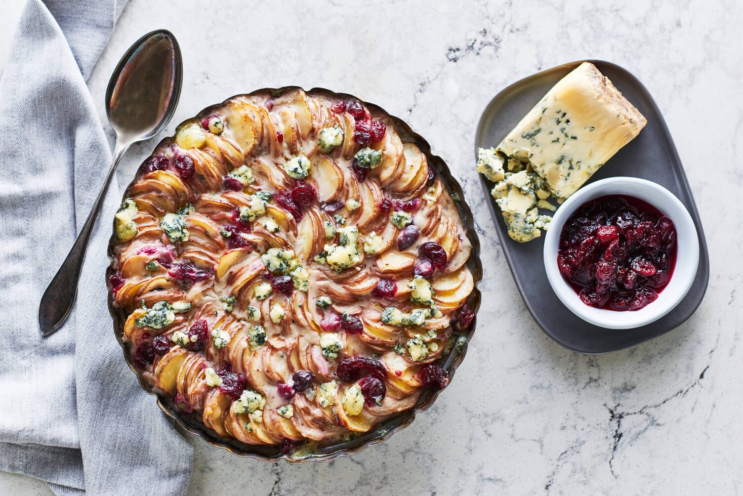 A nice pie dish full of beautifully arranged scalloped potatoes with cranberry sauce and stilton cheese on top.