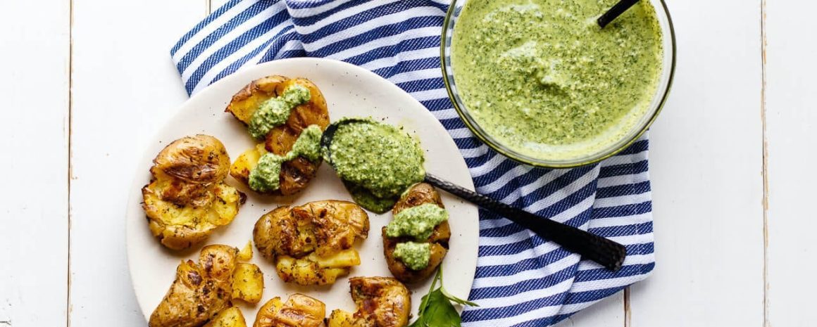 Grilled smashed fingerling potatoes on a plate with some dill dip on the side.