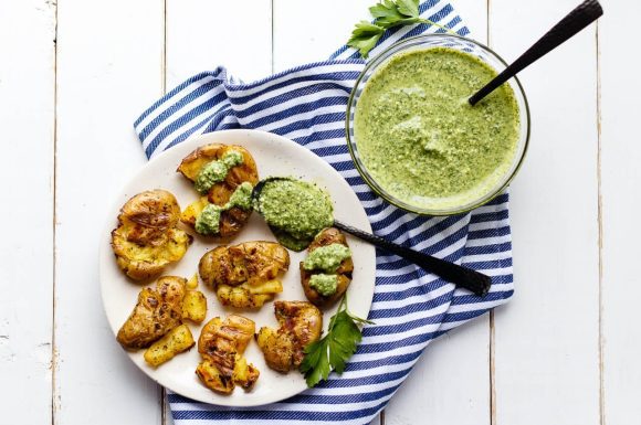 Grilled smashed fingerling potatoes on a plate with some dill dip on the side.