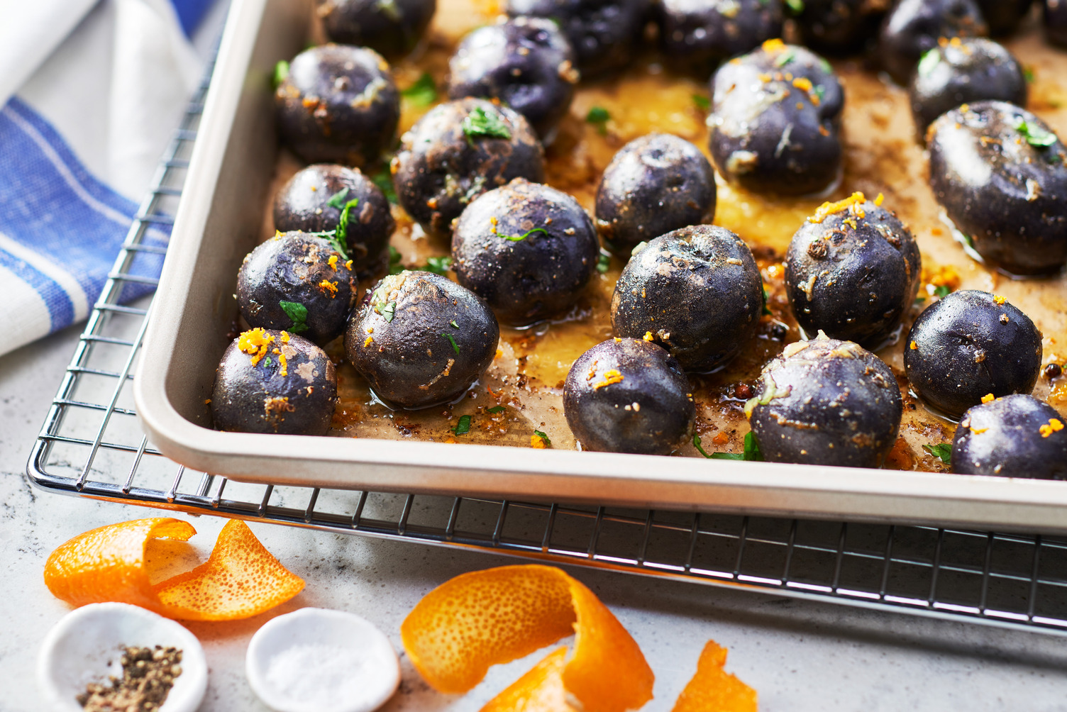 Purple potatoes with some orange zest on a roasting tray.