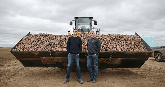 Two of our farmers in front of a tractor full of potatoes.