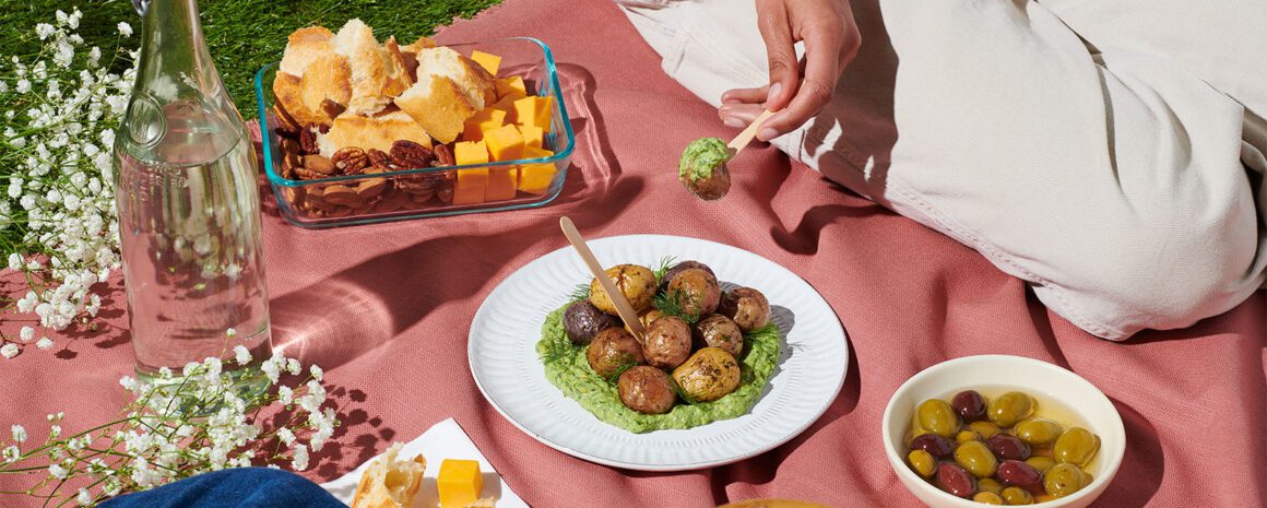 A picnic blanket with some plates of snacks and Little Potatoes with a creamy avocado dill dip.