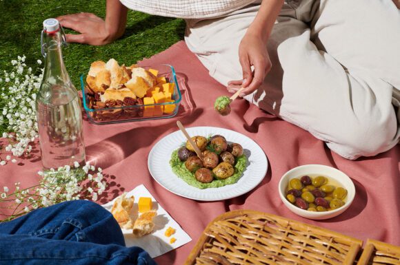 A picnic blanket with some plates of snacks and Little Potatoes with a creamy avocado dill dip.