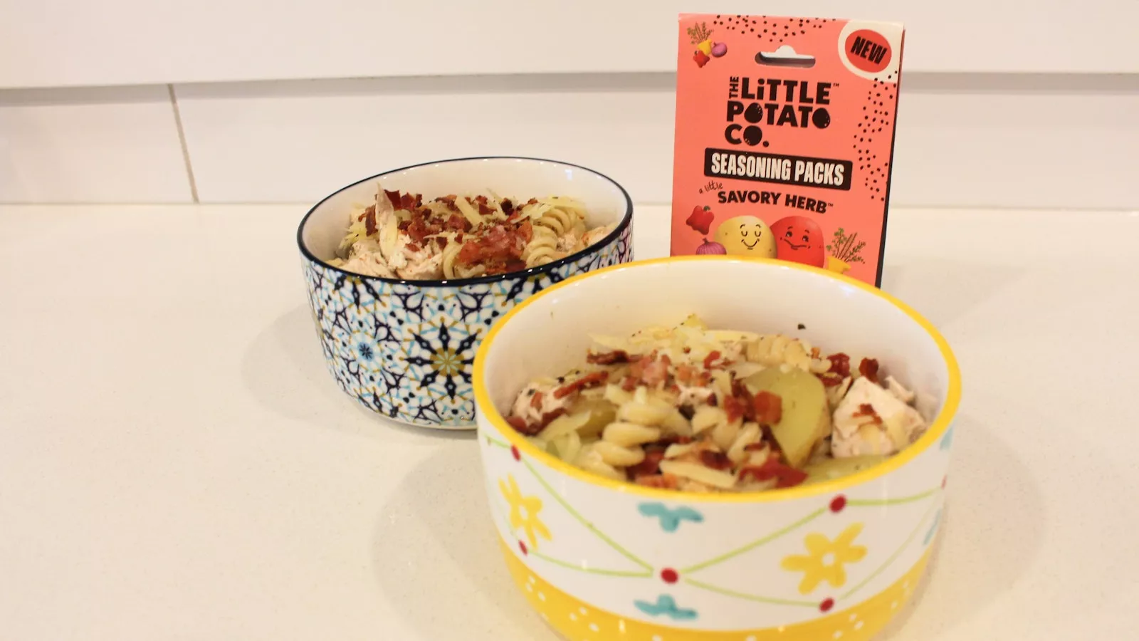 Two bowls of a potato pasta salad with chicken and veggies. A box of our seasoning packs are in the background.