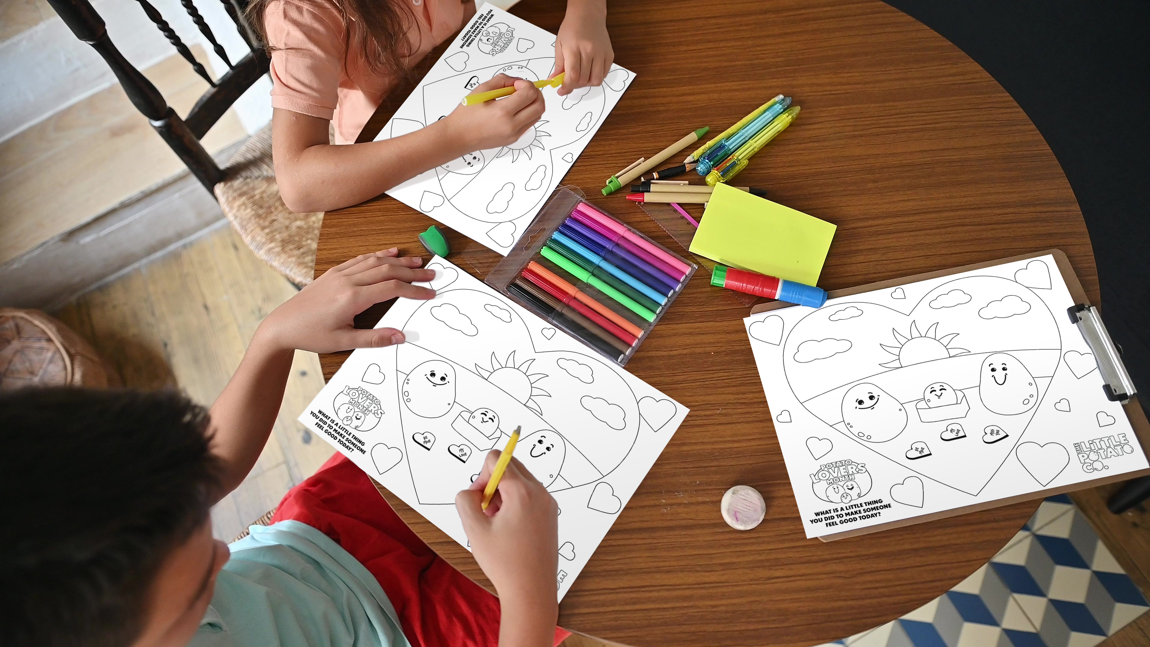 Kids coloring our Potato Lover's Month coloring pages around a table with some art supplies.