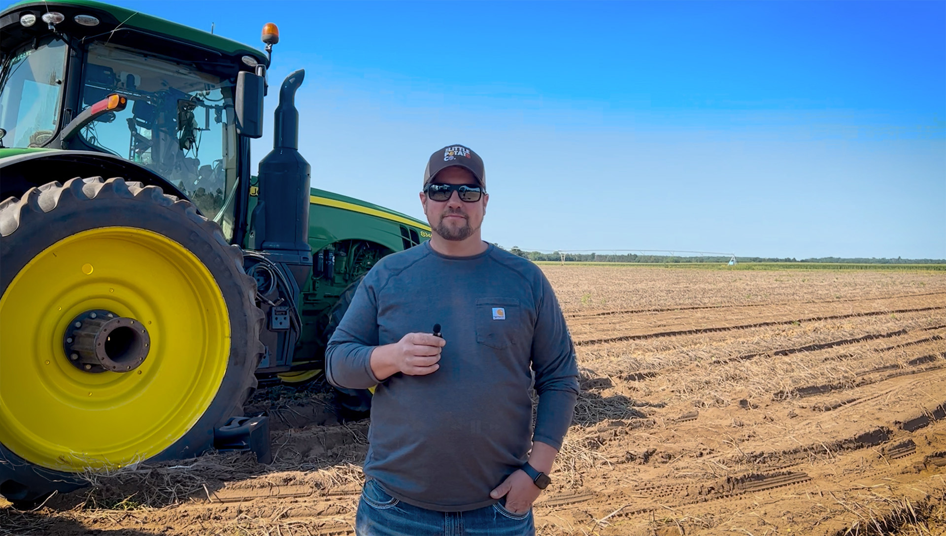 A farmer stands in front of a tractor on his field.