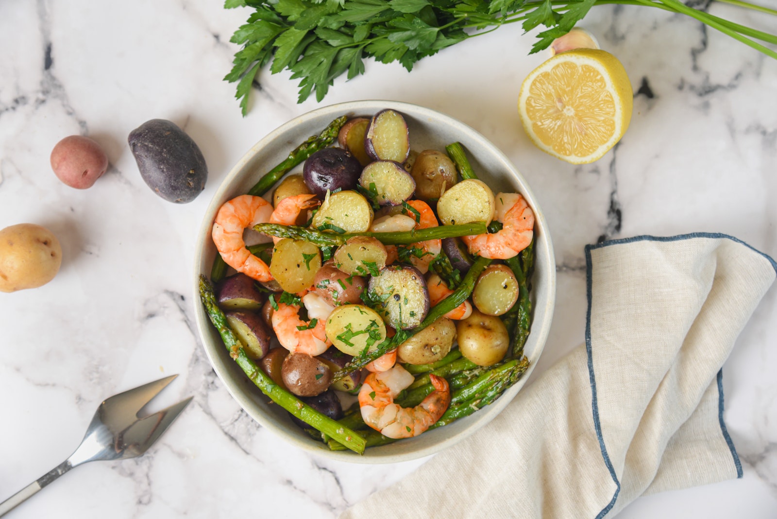 A bowl of shrimp and veggies and Little Potatoes on a white background.