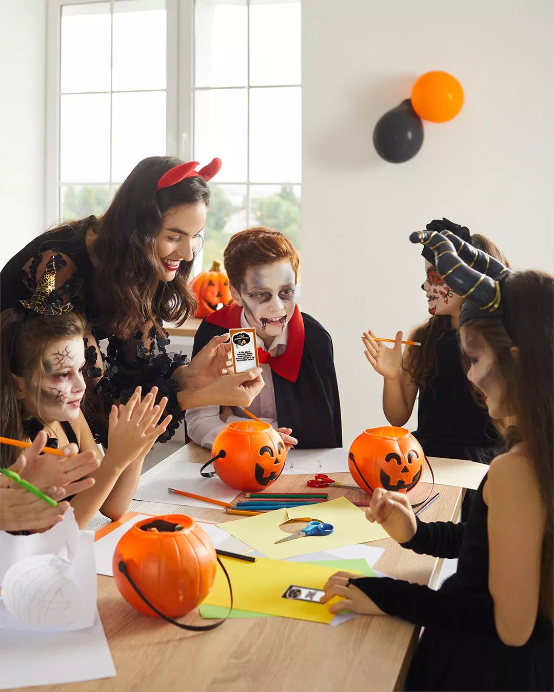 A group of children sit around a table dressed in Halloween costumes coloring together.