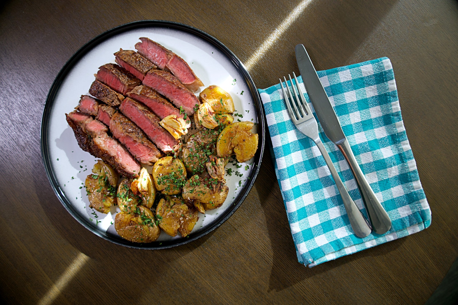 A plate of deliciously medium-rare ribeye steak with some smashed Little Potatoes on the side.