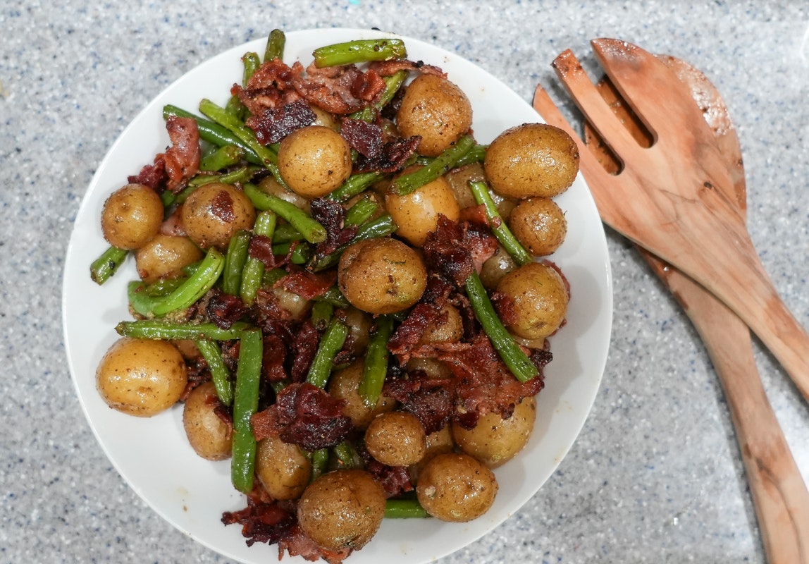 A plate of A Little Homestyle Ranch™ Little Potatoes on a white plate with some green beans and bacon.