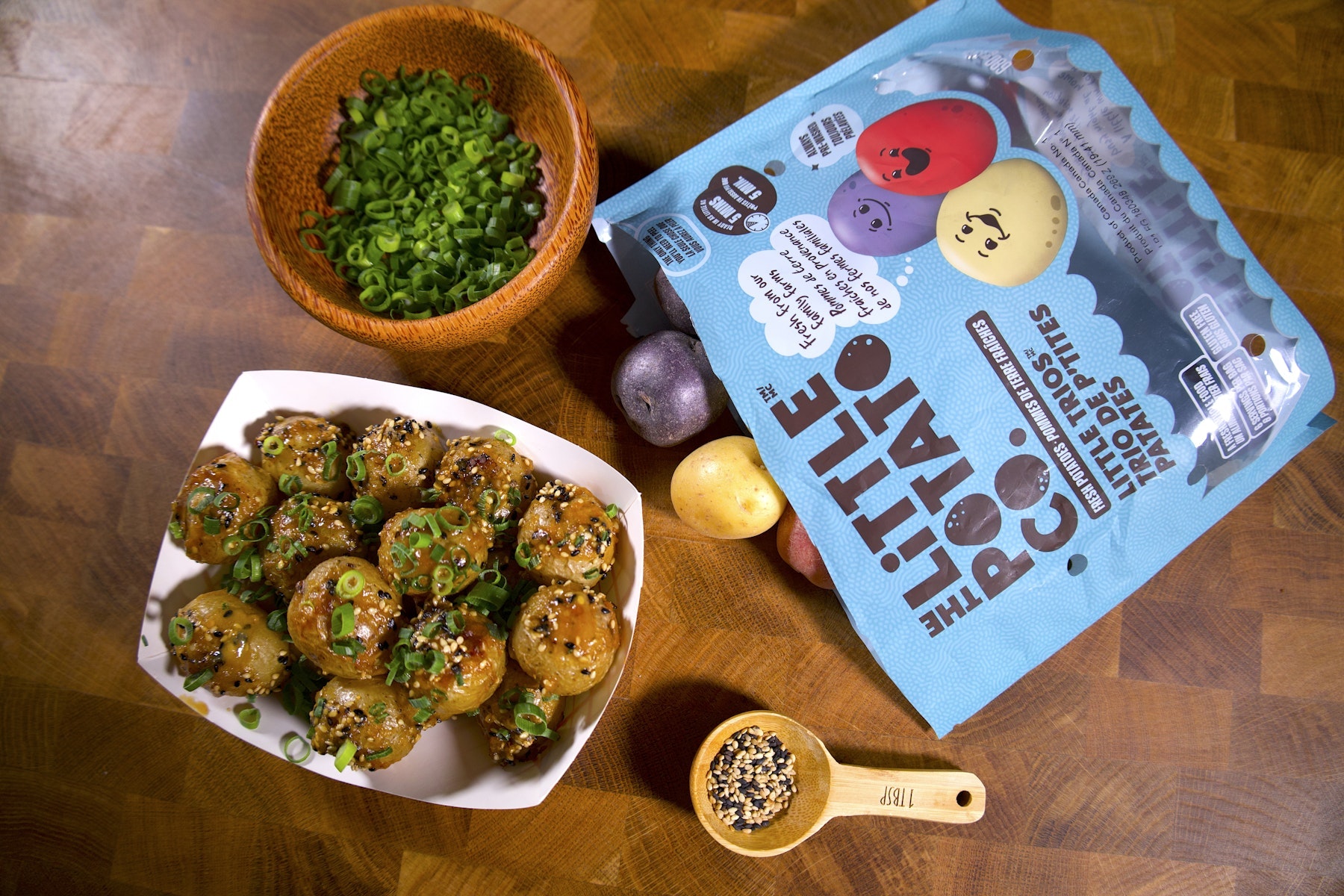 A bag of Little Trios® next to some spices in bowls and a small platter of Little Potatoes covered in Japanese miso butter.