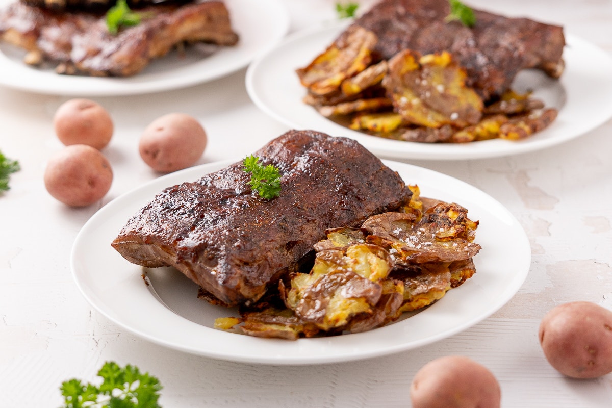 A plate of sous vide made baby back ribs with smashed potatoes next to them.
